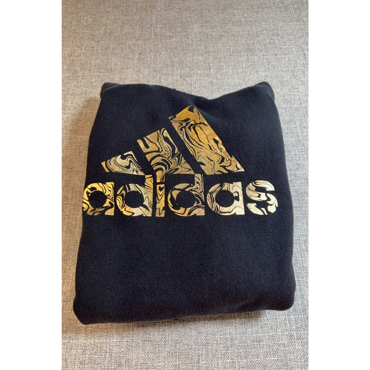 Second Half Supply Co, LLC Adidas black hoodie with metallic gold marbled logo graphic folded on a grey surface.