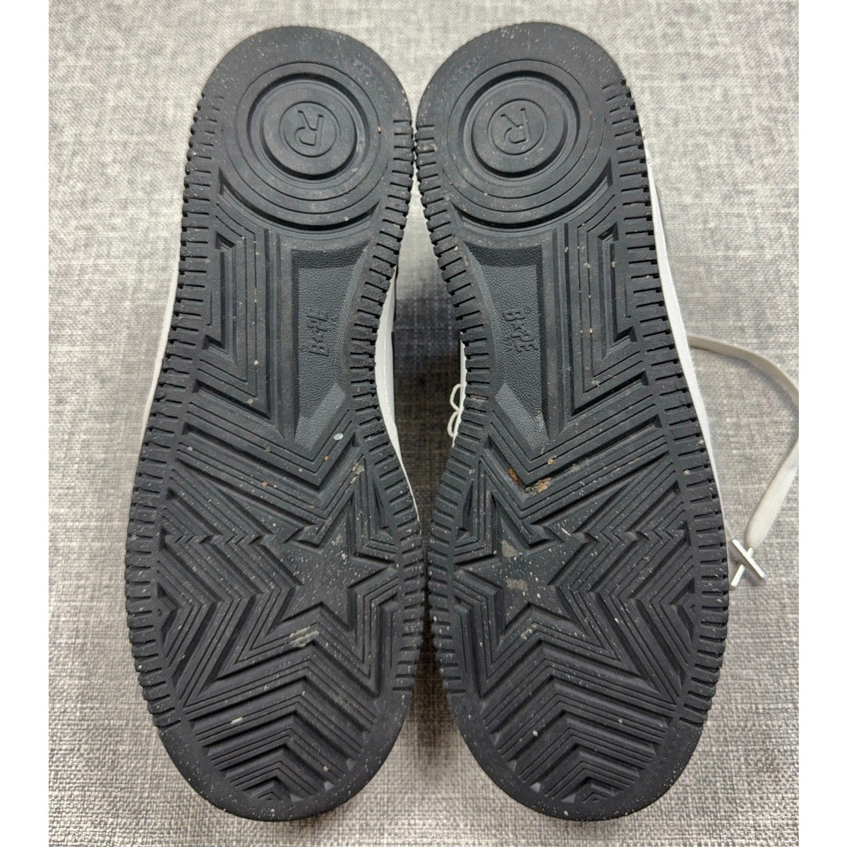 Second Half Supply Co, LLC black rubber outsoles of BAPE STA low-top sneakers featuring star and logo tread patterns.
