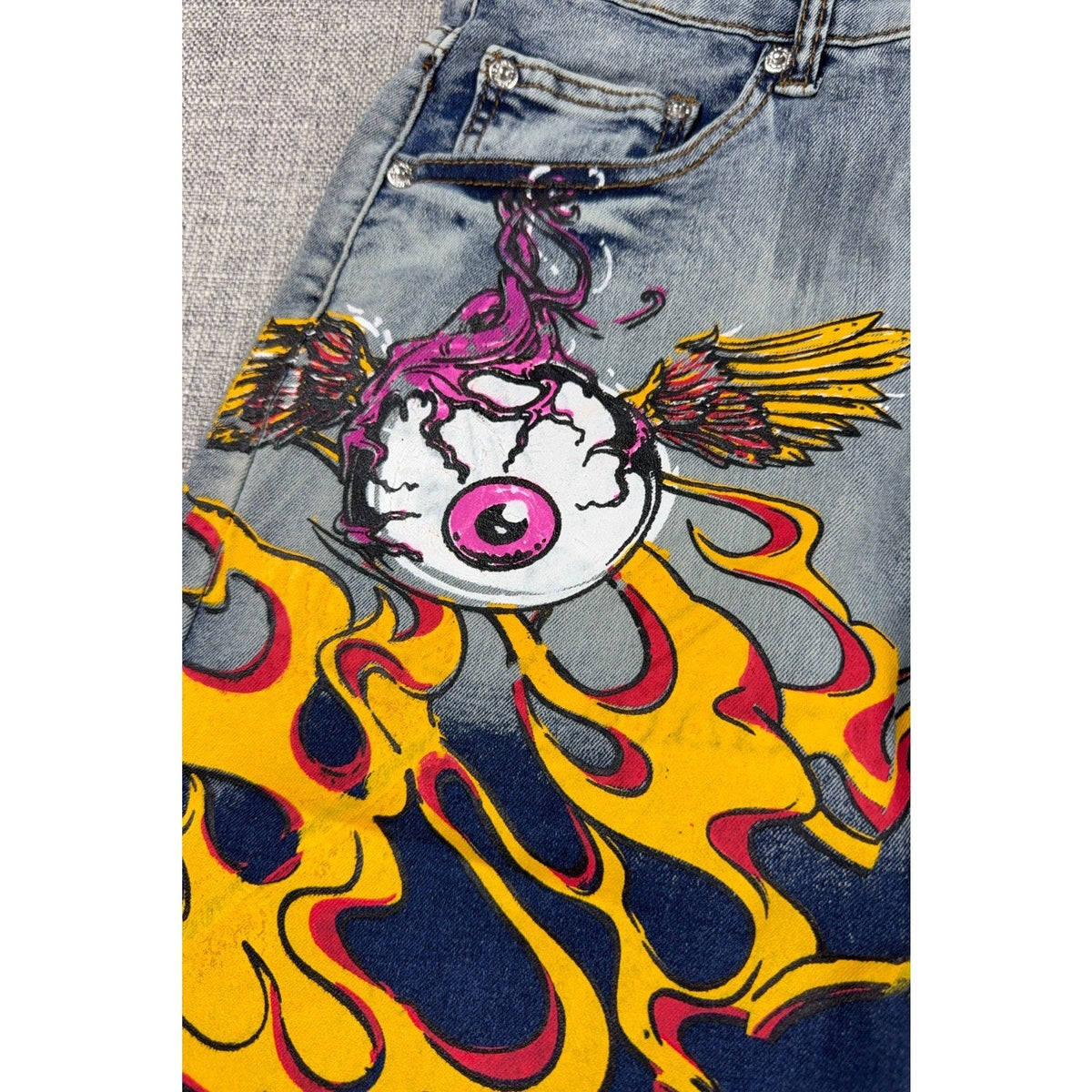 Second Half Supply Co, LLC light-wash denim shorts featuring a winged eyeball and yellow flame graphic design