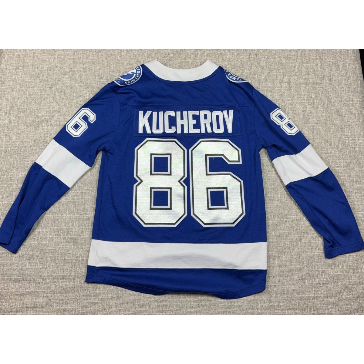 Second Half Supply Co, LLC blue and white Tampa Bay Lightning Nikita Kucherov #86 hockey jersey, back view.