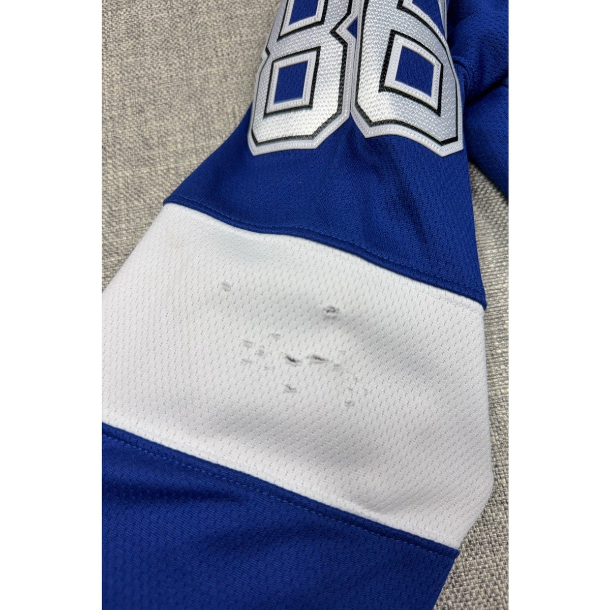 Second Half Supply Co, LLC blue and white Tampa Bay Lightning hockey jersey sleeve showing fabric snags and holes