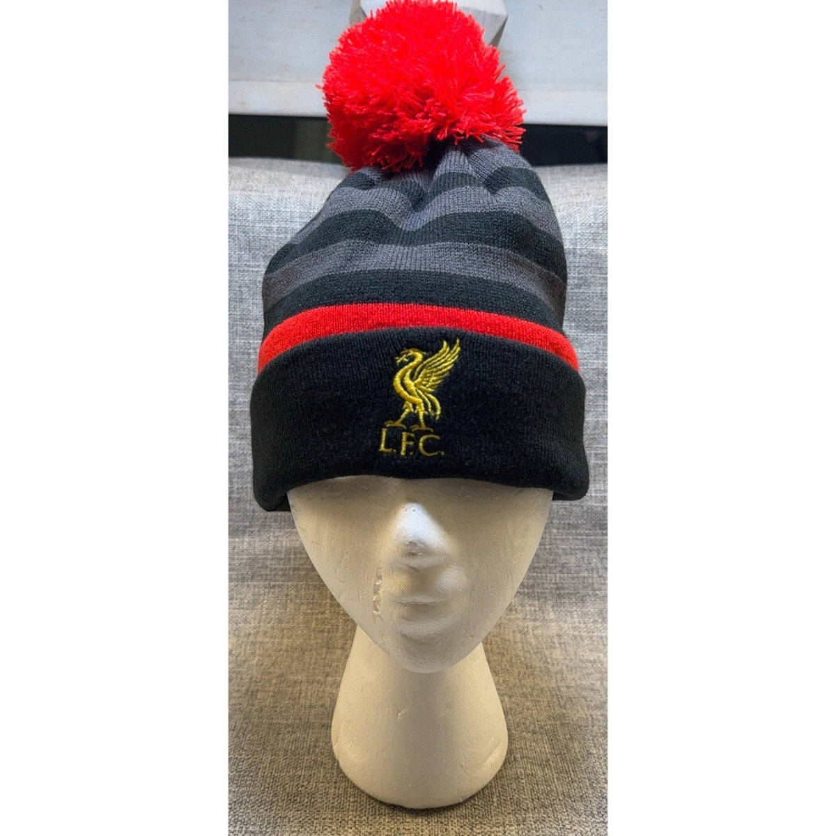 Second Half Supply Co, LLC Liverpool FC Warrior knit beanie with red pom-pom, black and gray stripes, and gold logo.