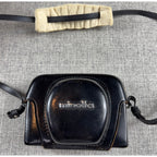 Second Half Supply Co, LLC vintage black leather Minolta Hi-Matic 11 camera case with shoulder strap on grey fabric