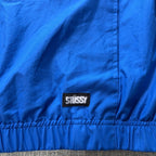 Second Half Supply Co, LLC blue Stussy windbreaker jacket featuring a woven brand label on the elastic hem