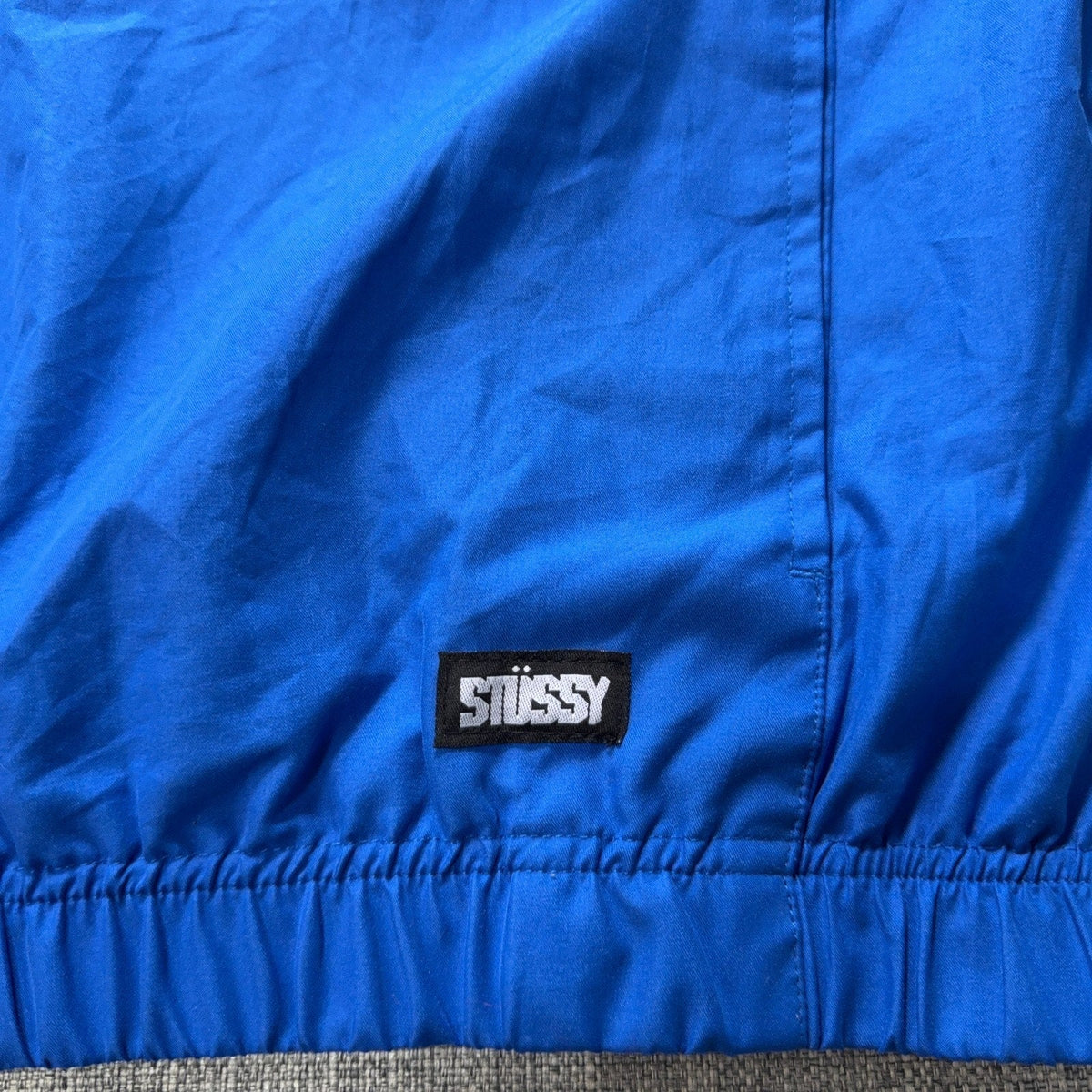 Second Half Supply Co, LLC blue Stussy windbreaker jacket featuring a woven brand label on the elastic hem