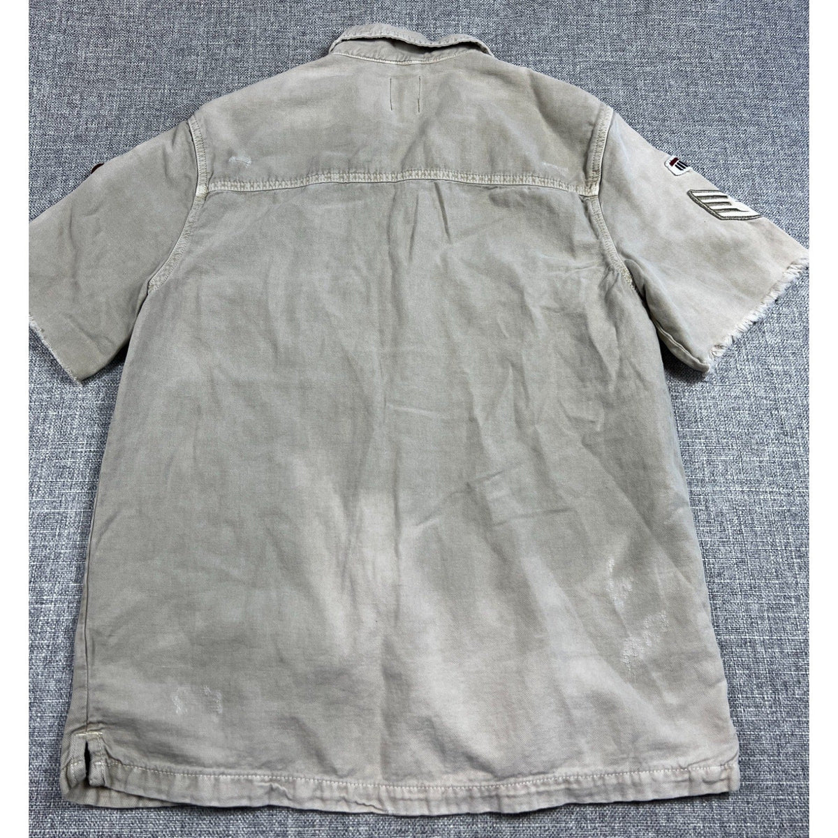 Back view of a Second Half Supply Co, LLC Zara khaki utility shirt with raw sleeve hems and military patches.